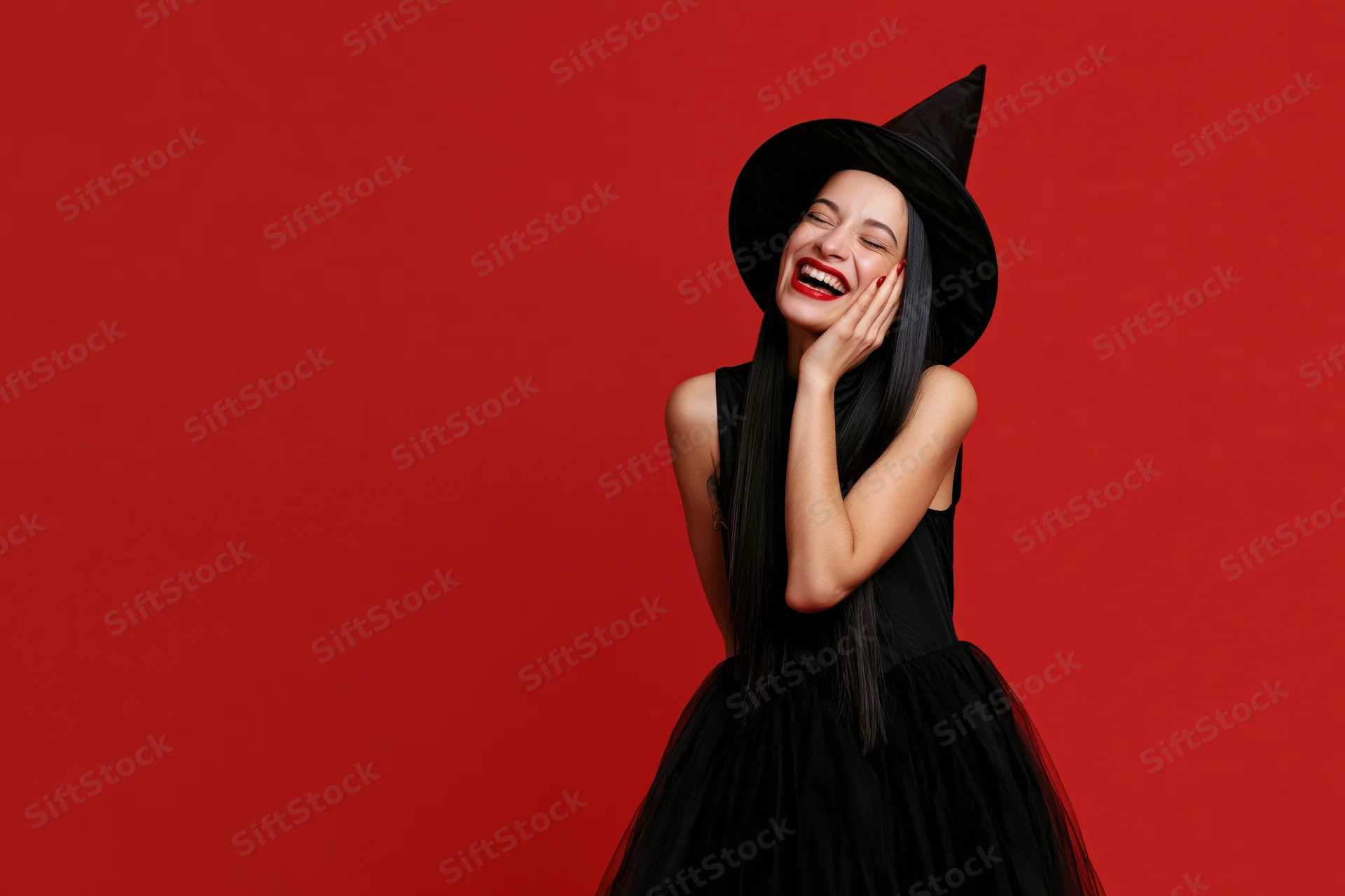 Woman in witch costume laughing with hand on face against red background
