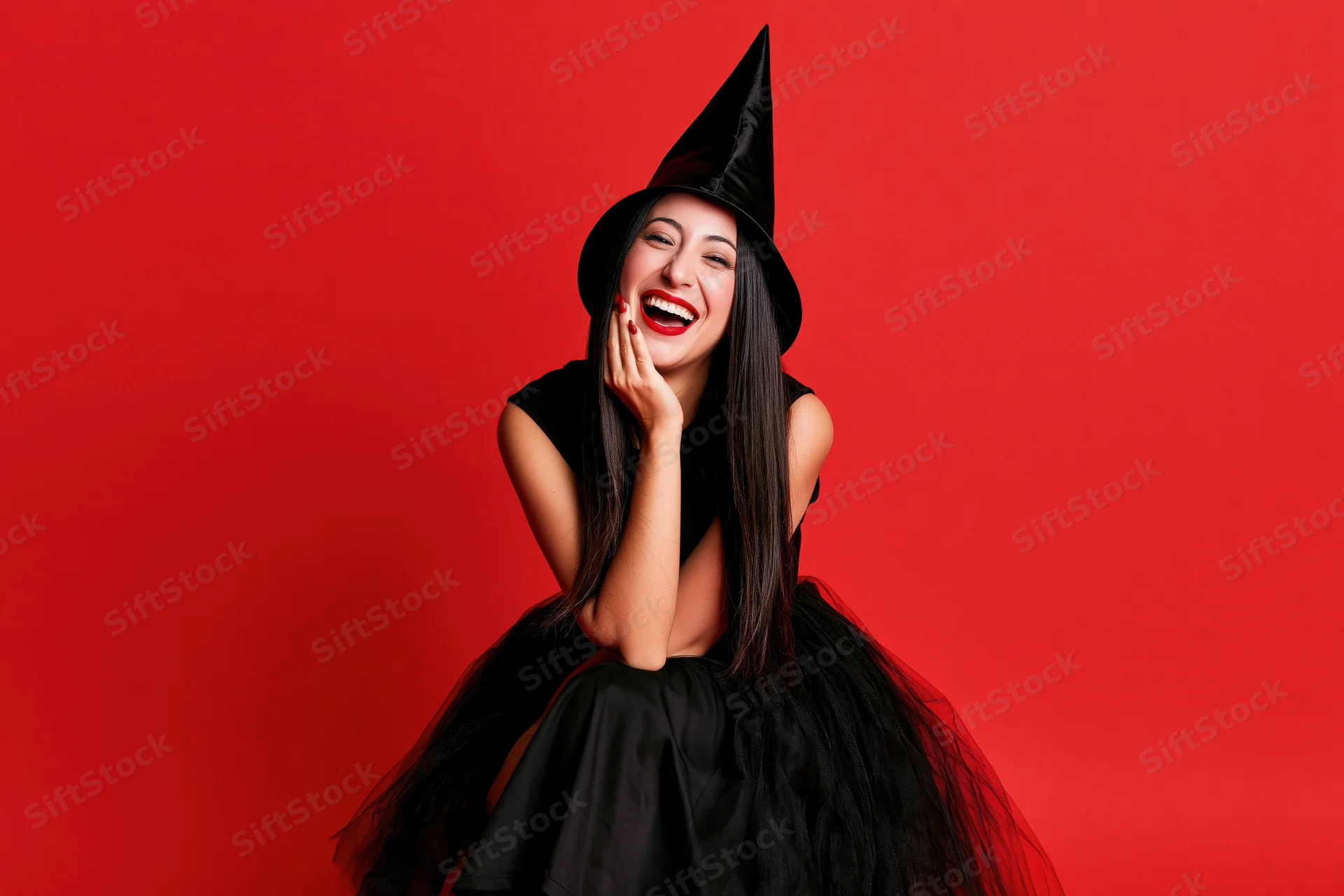 Woman in witch costume laughing with hand on cheek against red background