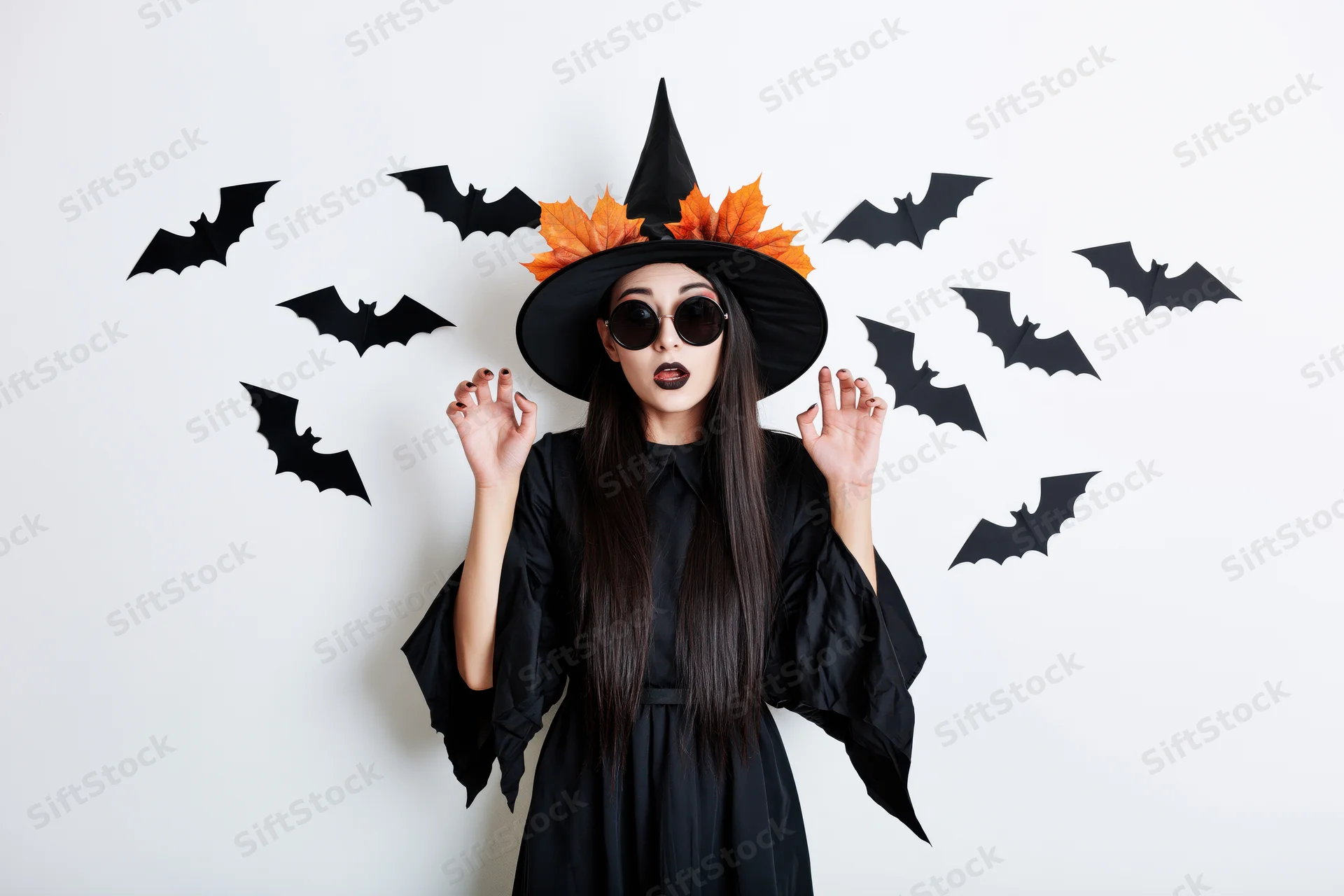 Woman in witch costume with surprised expression surrounded by paper bats on white background