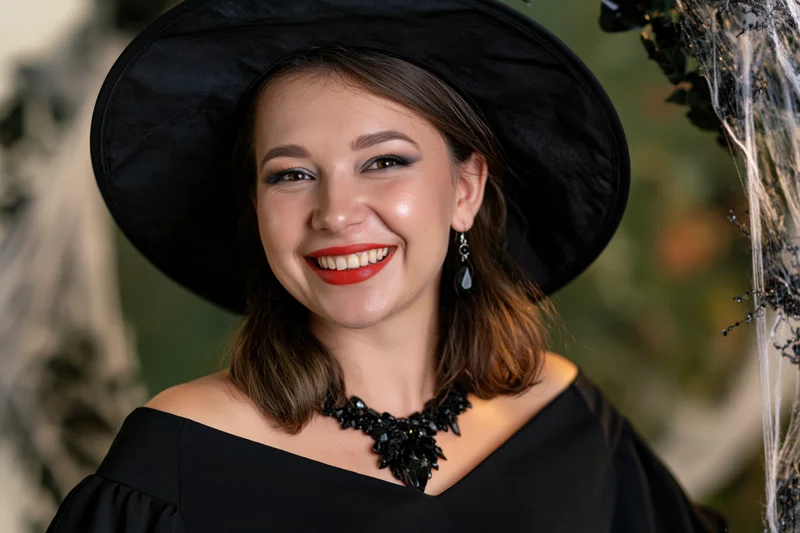 Young woman in black witch hat smiling with jewelry and costume details outdoors
