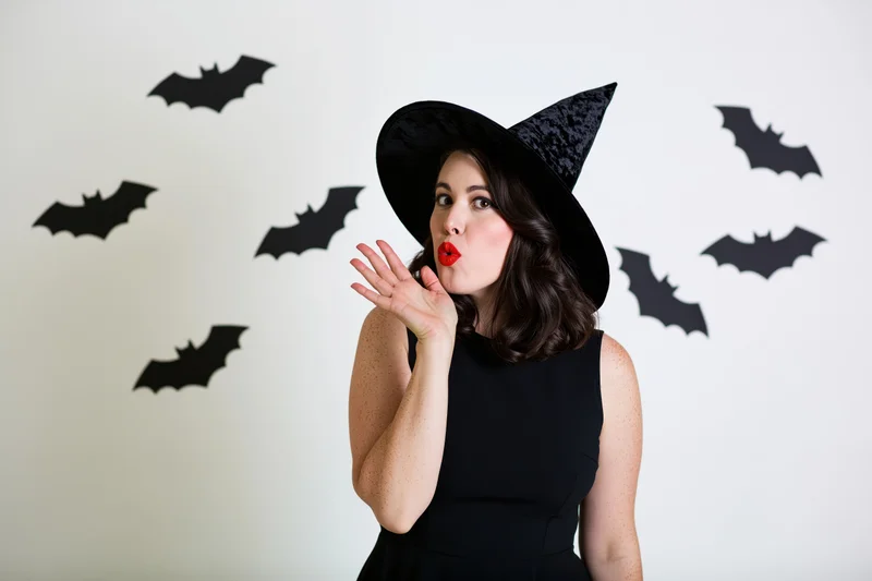 Woman in witch costume blowing a kiss in front of bat-decorated wall