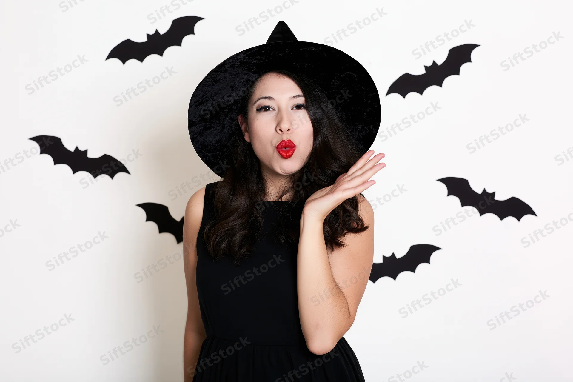 Woman in witch costume blowing a kiss with bat decorations on white wall