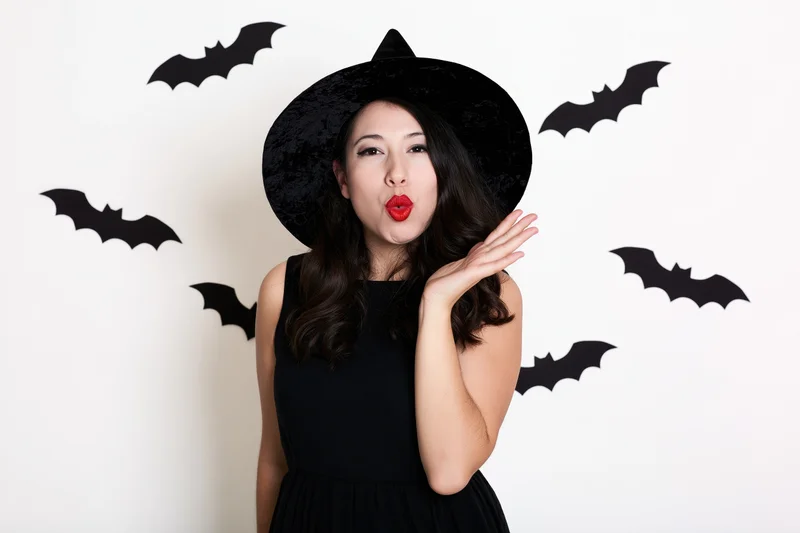 Woman in witch costume blowing a kiss with bat decorations on white wall
