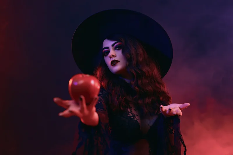Woman in witch costume holding red apple in smoky dark setting