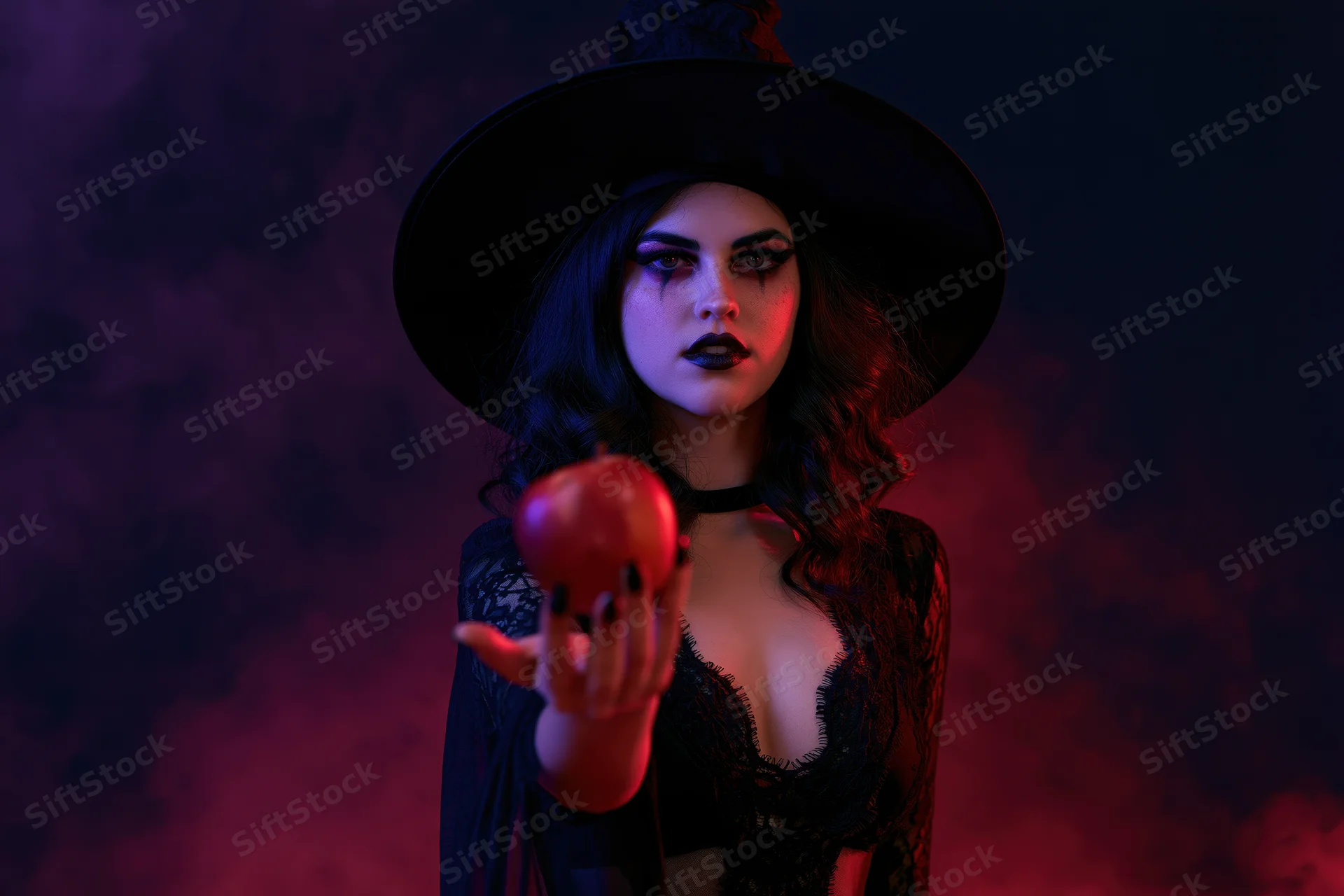 Woman in witch costume holding red apple in smoky neon-lit setting