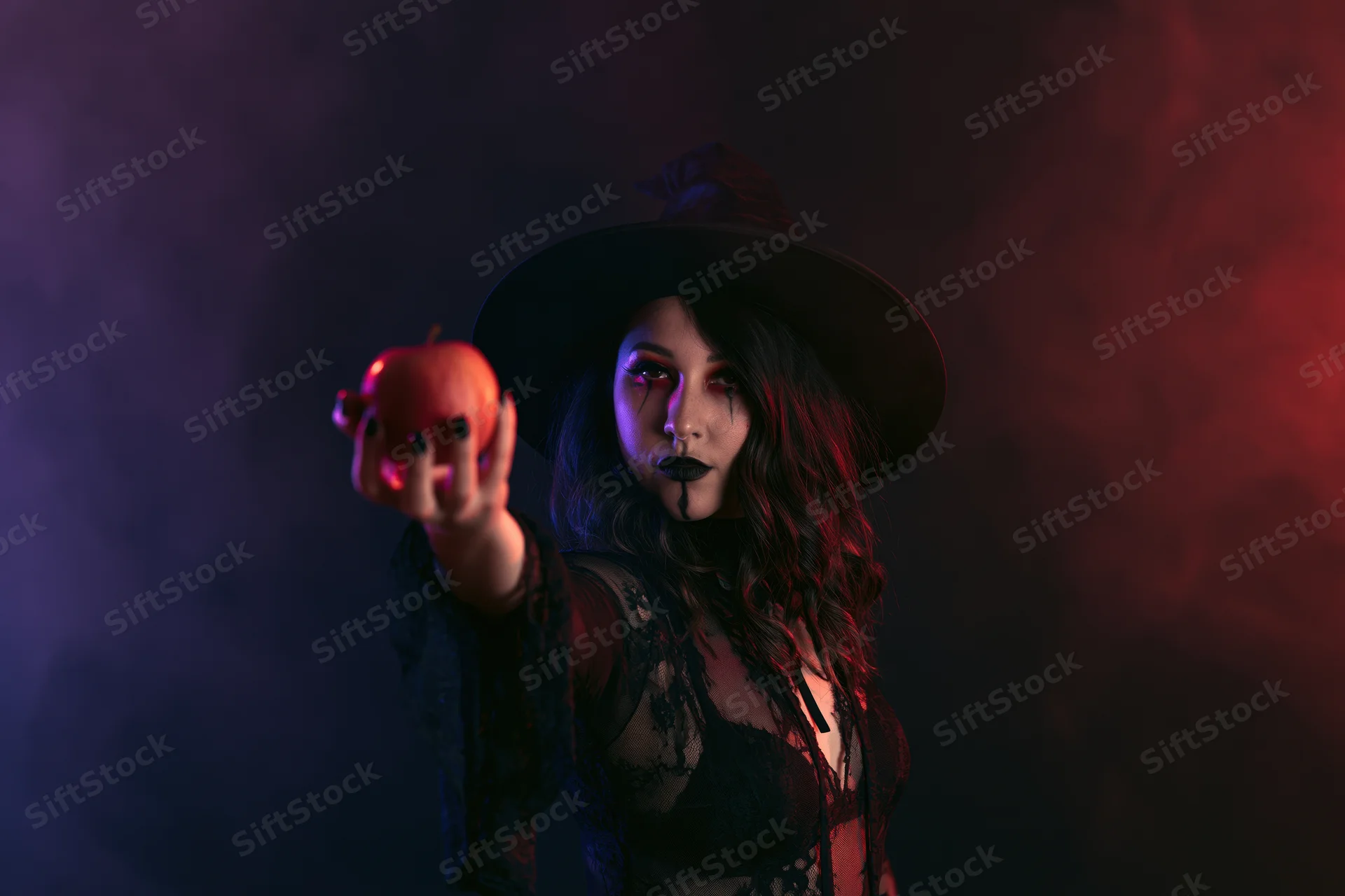 Woman in witch costume holding red apple in smoky studio setting