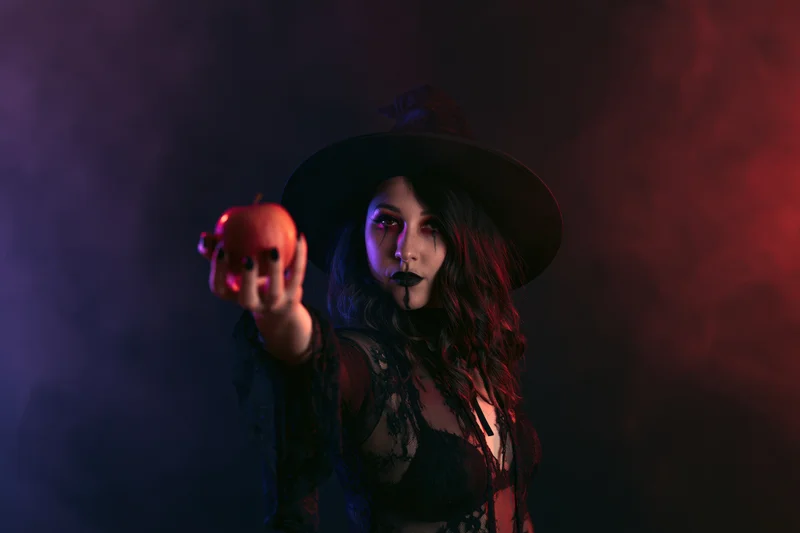Woman in witch costume holding red apple in smoky studio setting