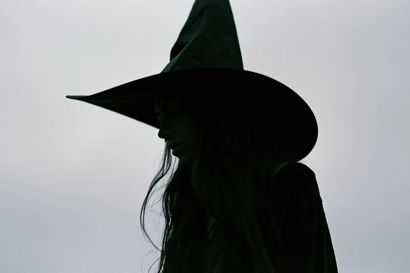 Woman in witch silhouette with pointed hat in profile against overcast sky