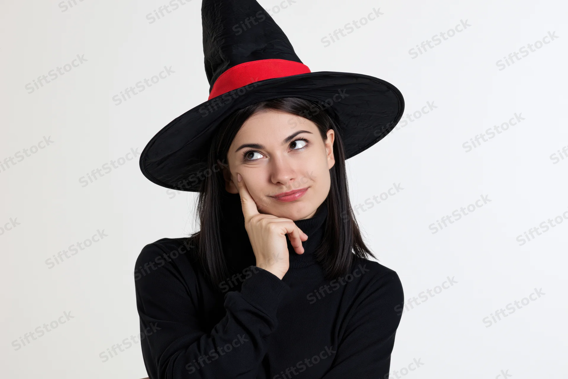 Young woman in witch costume with hand on chin against white background
