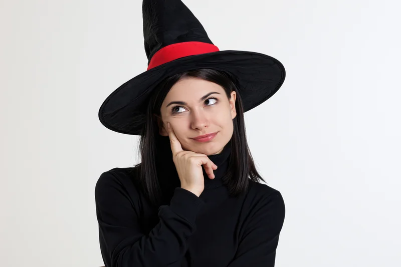 Young woman in witch costume with hand on chin against white background