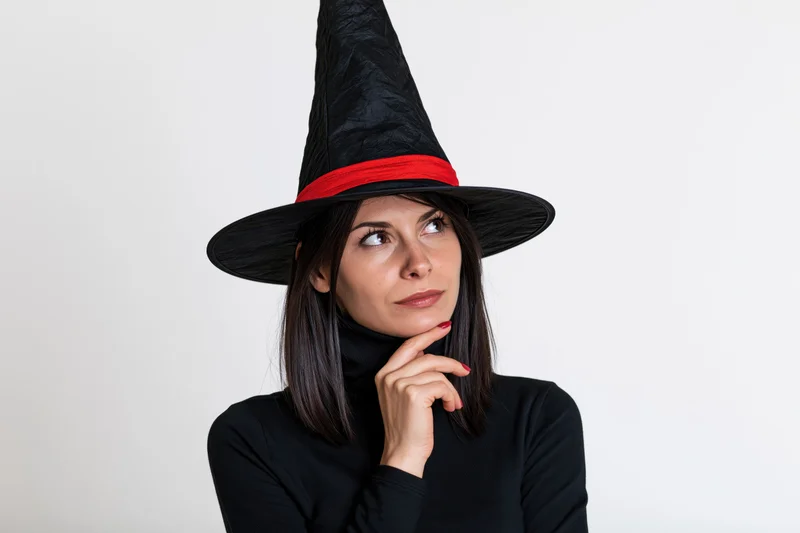 Woman in witch hat thinking with hand on chin against white background