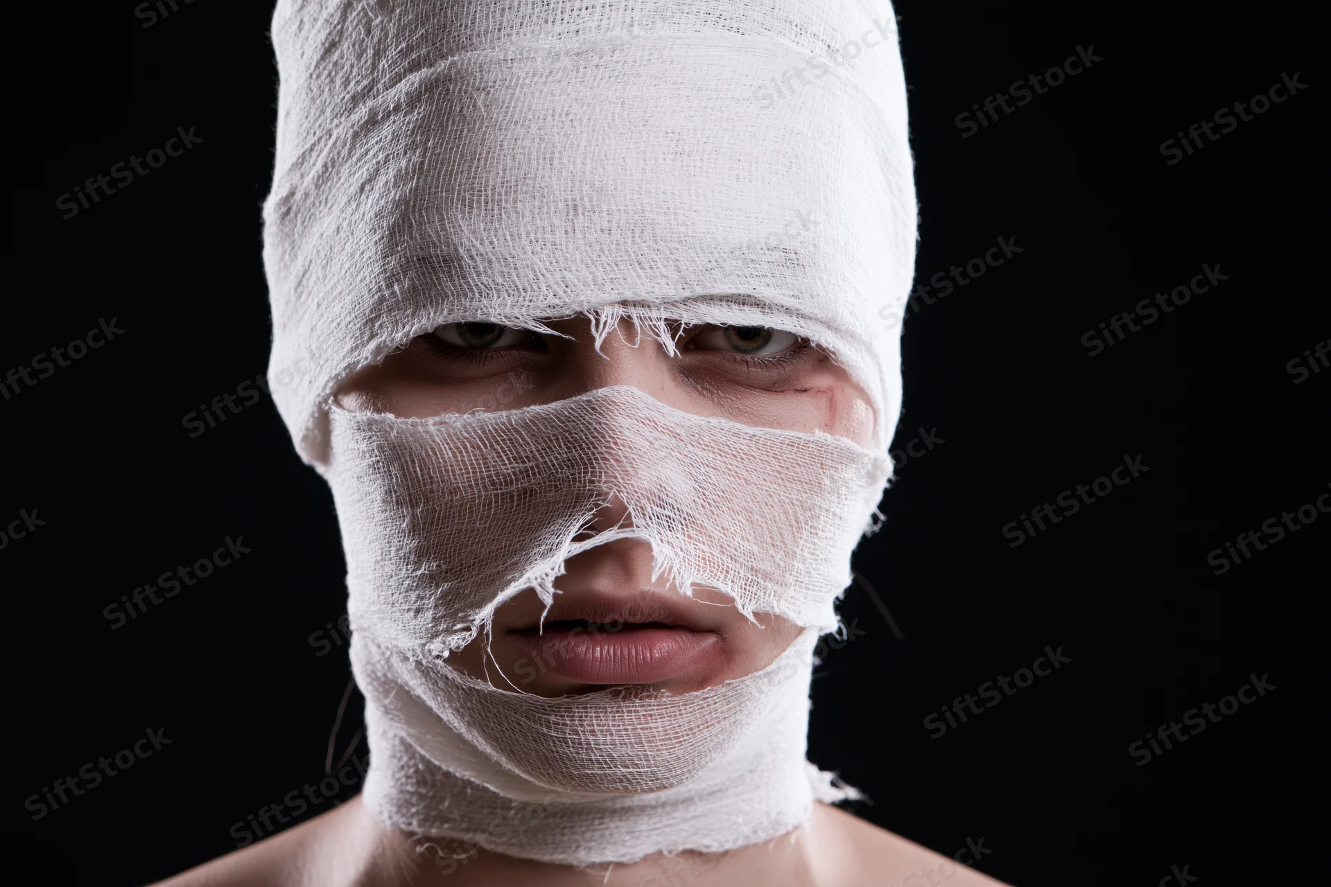 Woman with face and head wrapped in white bandages against black background