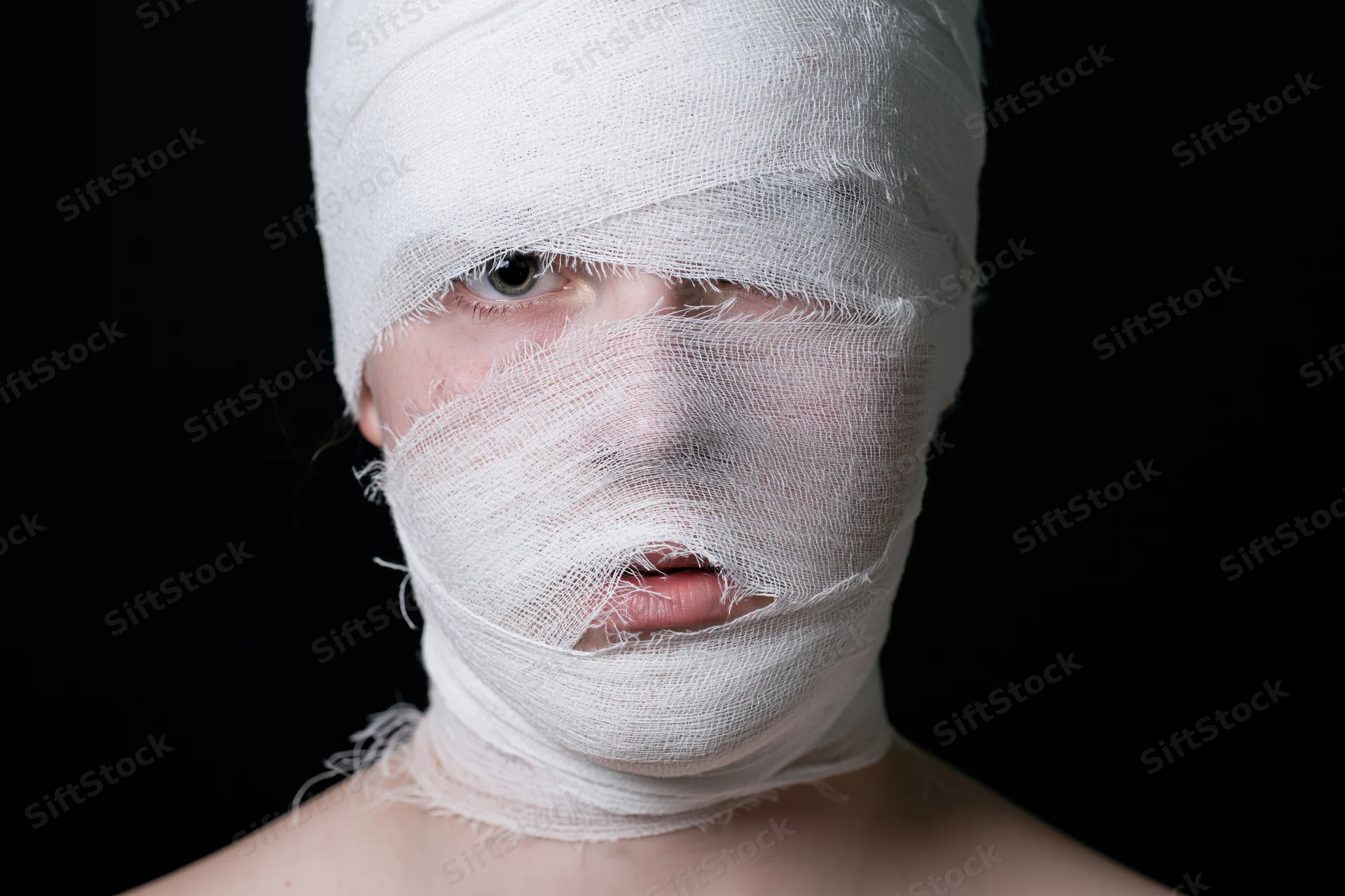 Woman with face and head wrapped in white bandages against black background