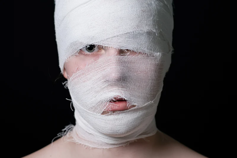 Woman with face and head wrapped in white bandages against black background