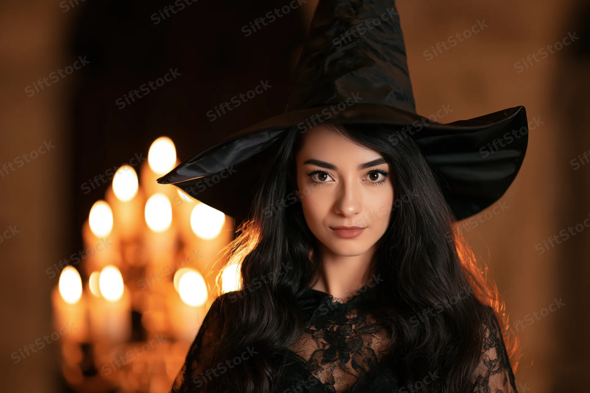 Woman in witch costume with tall black hat and lace dress, lit by candles in dim room