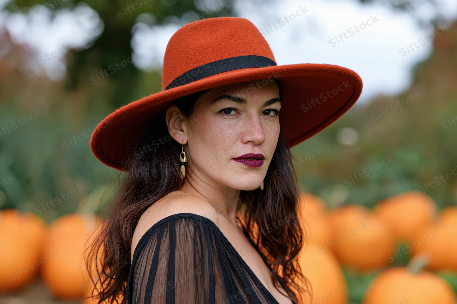 Woman in orange hat and black sheer dress standing in pumpkin field