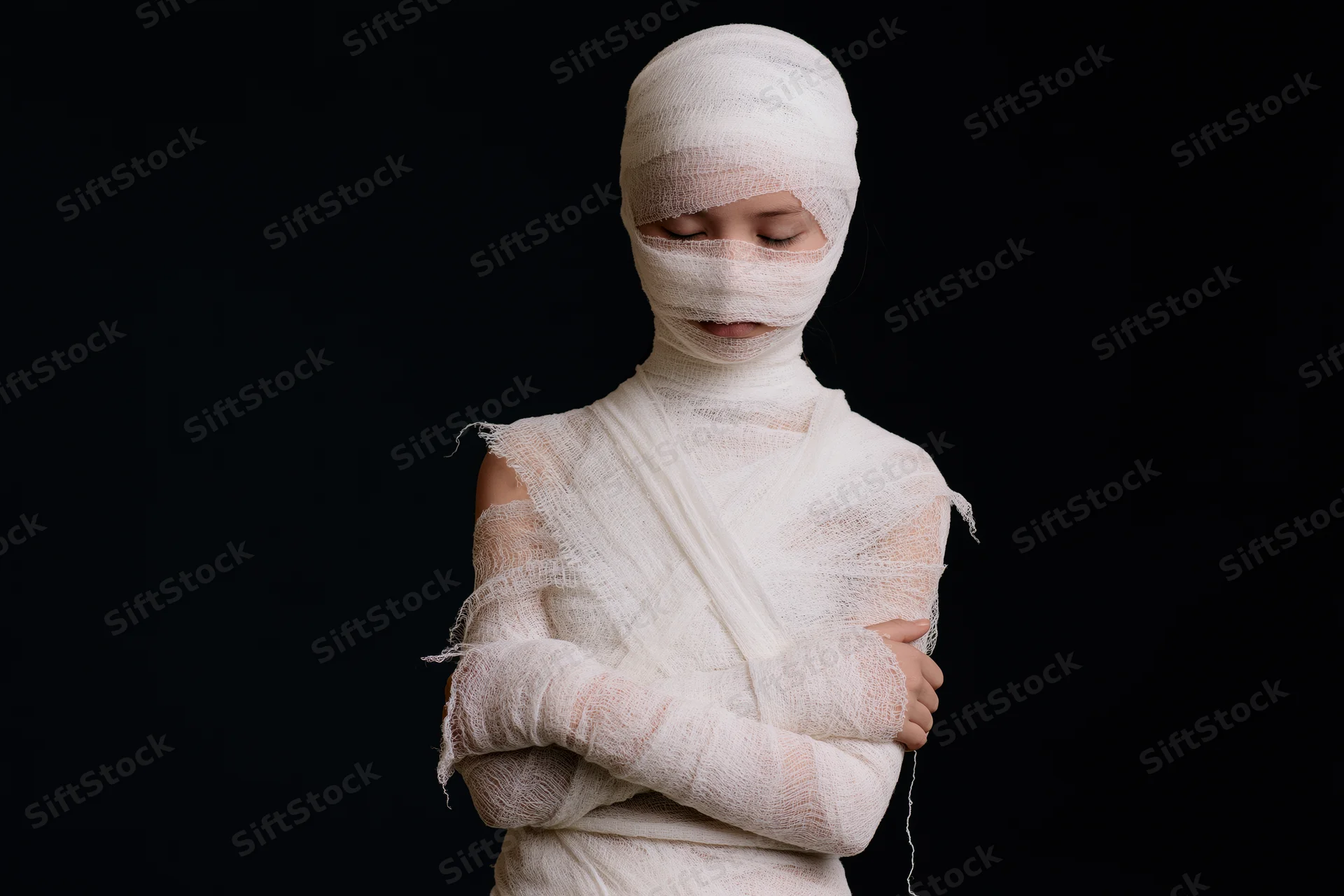 Young woman wrapped in white gauze bandages with arms crossed against black background