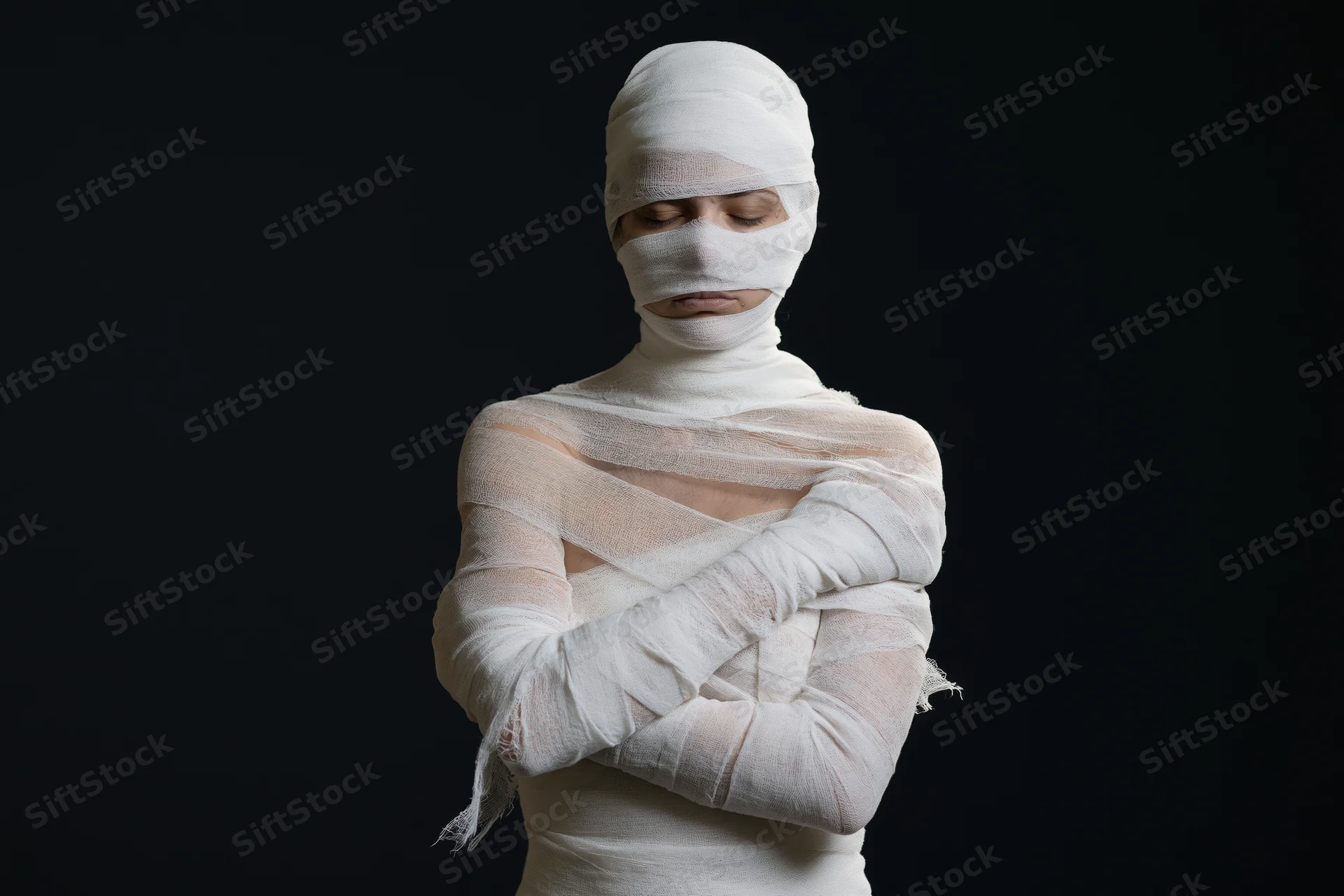 Woman wrapped in white gauze bandages with arms crossed against black background