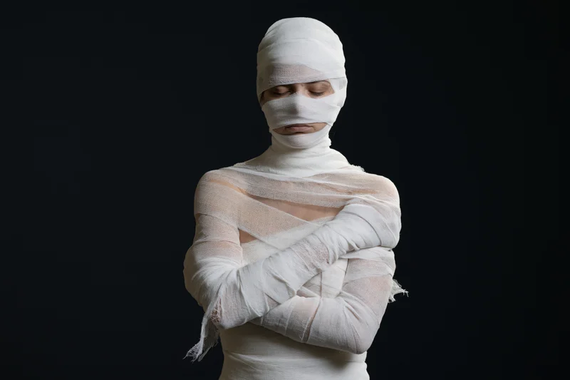 Woman wrapped in white gauze bandages with arms crossed against black background