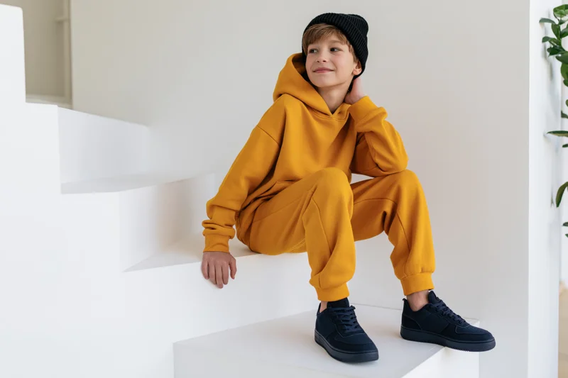 Boy in yellow hoodie and black beanie sitting on white stairs indoors