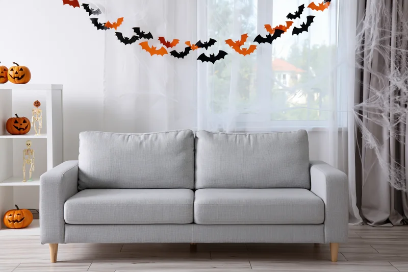 Light grey sofa in a bright living room decorated with halloween pumpkins, bats, and spiderwebs