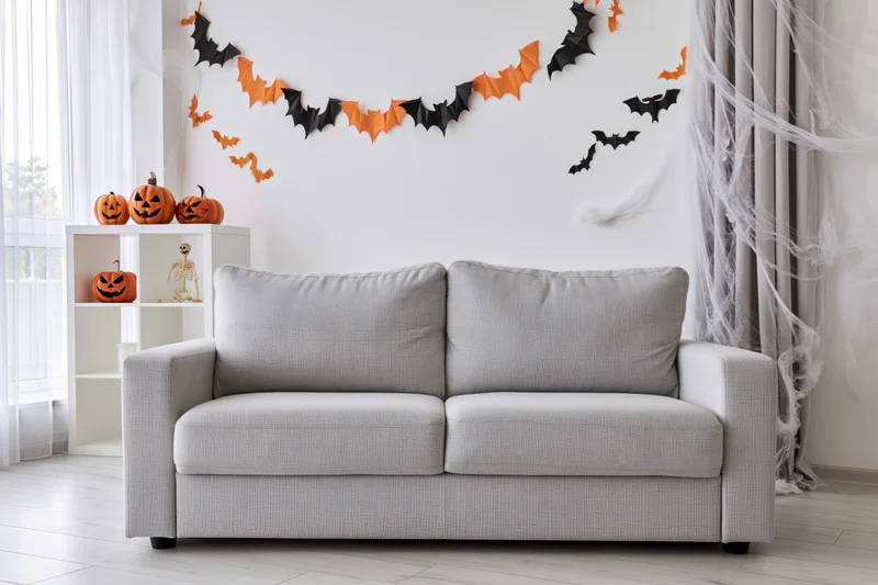 Light grey sofa in a bright living room decorated with halloween pumpkins, bats, and cobwebs