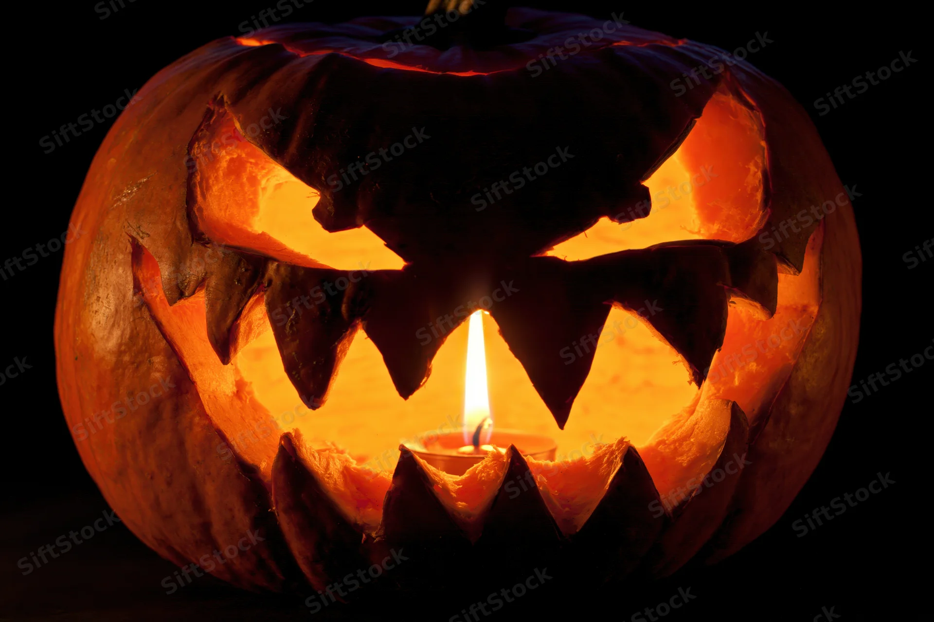 Carved pumpkin with jagged features glowing from within at night