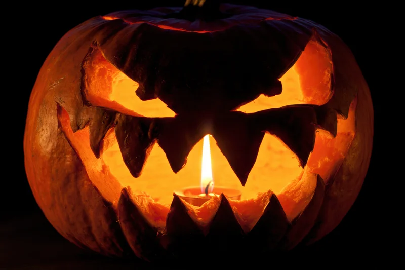 Carved pumpkin with jagged features glowing from within at night
