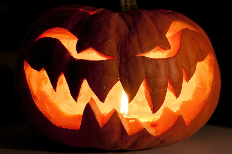 Carved pumpkin with jagged face glowing from within at night