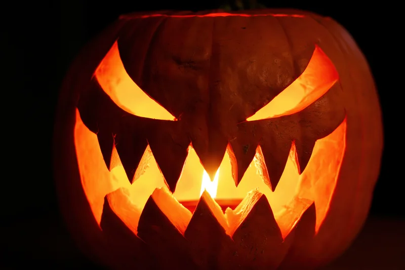 Carved pumpkin with jagged face glowing from within at night