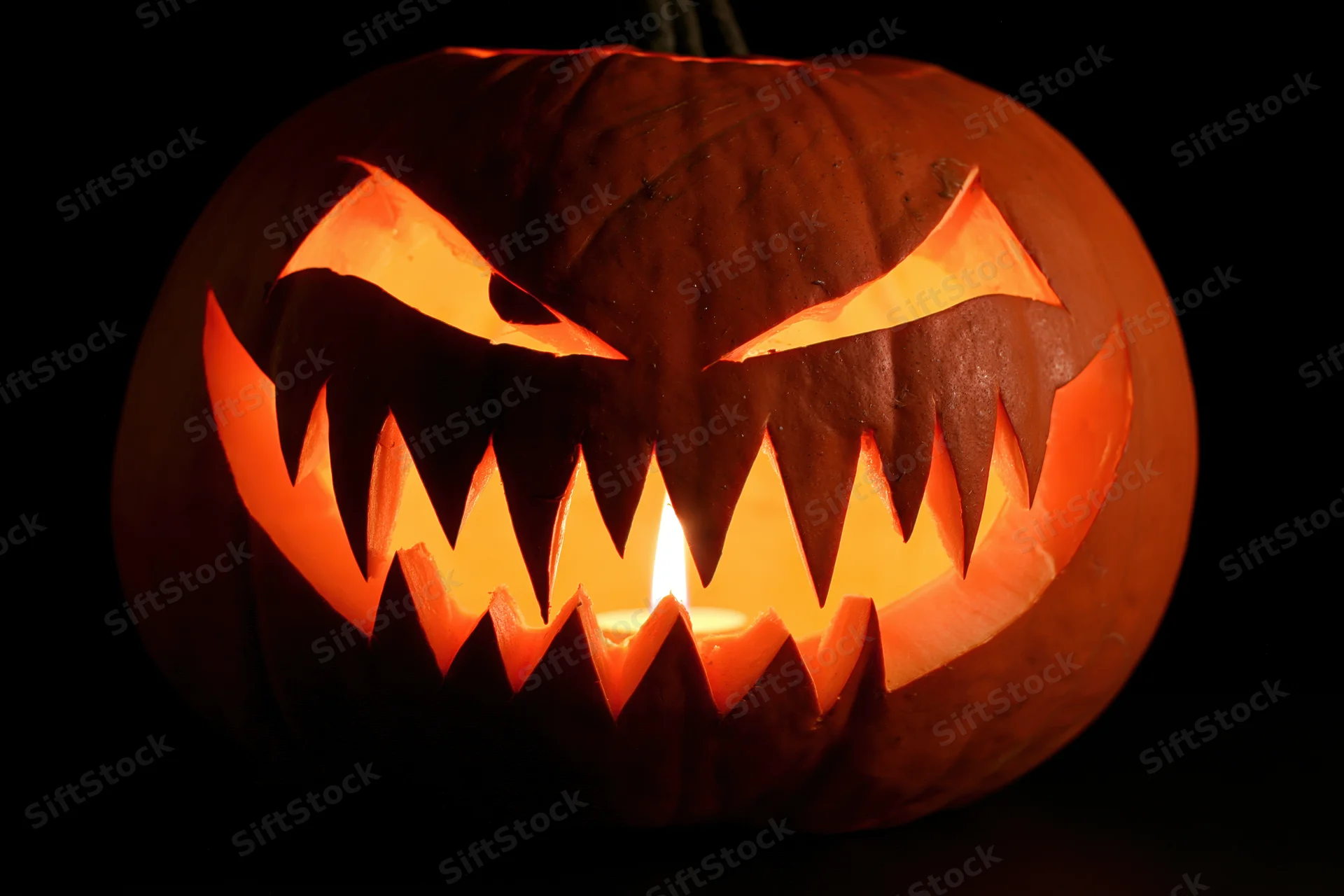Carved pumpkin with jagged teeth and glowing eyes lit from within against dark background
