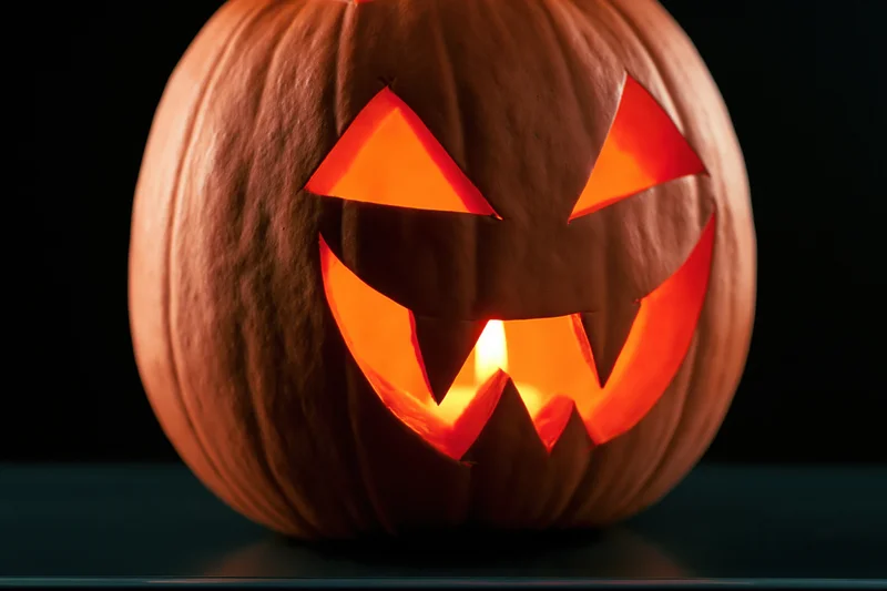 Carved pumpkin with glowing face on dark surface