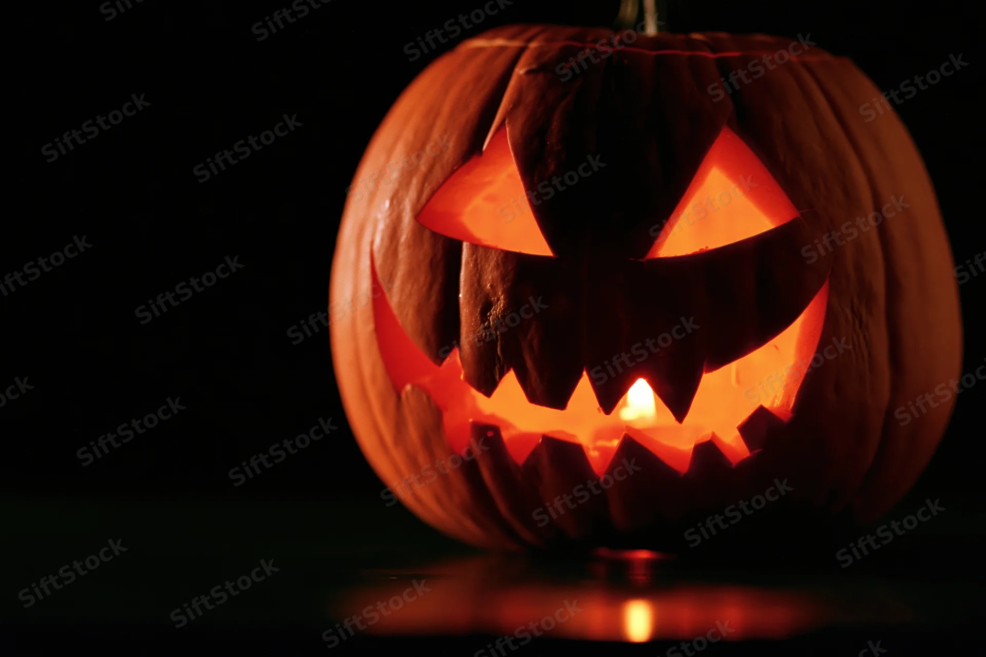 Carved pumpkin glowing from within on dark surface