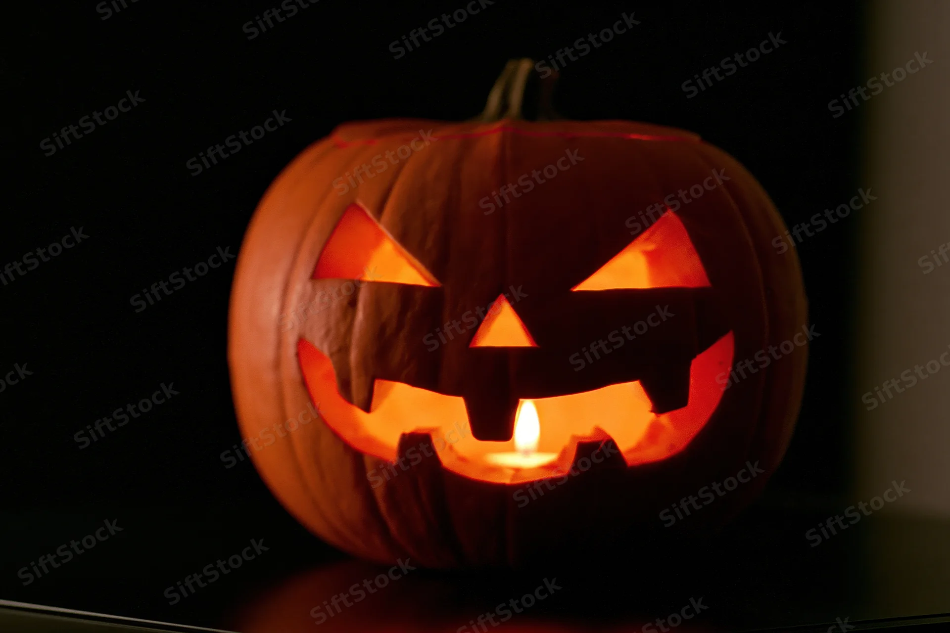 Carved pumpkin with glowing face lit by candle inside, placed on dark surface at night