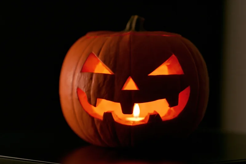 Carved pumpkin with glowing face lit by candle inside, placed on dark surface at night