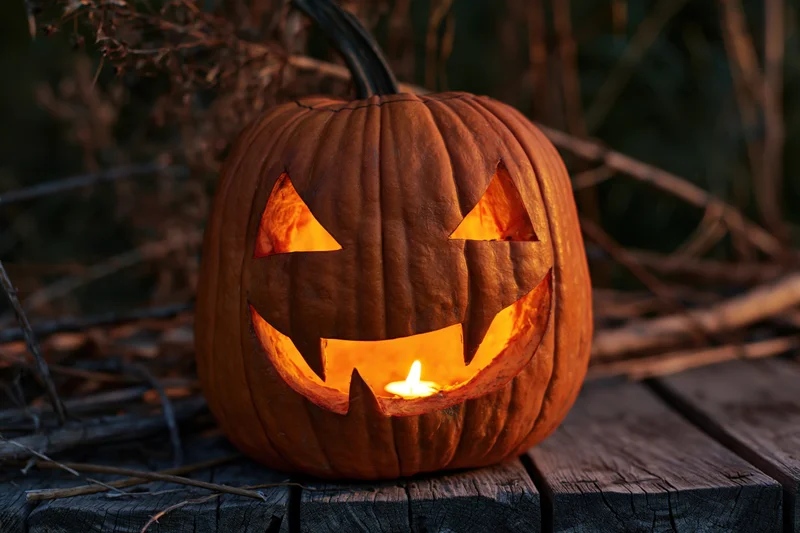 Carved pumpkin with glowing candle inside sitting on wooden table outdoors at night