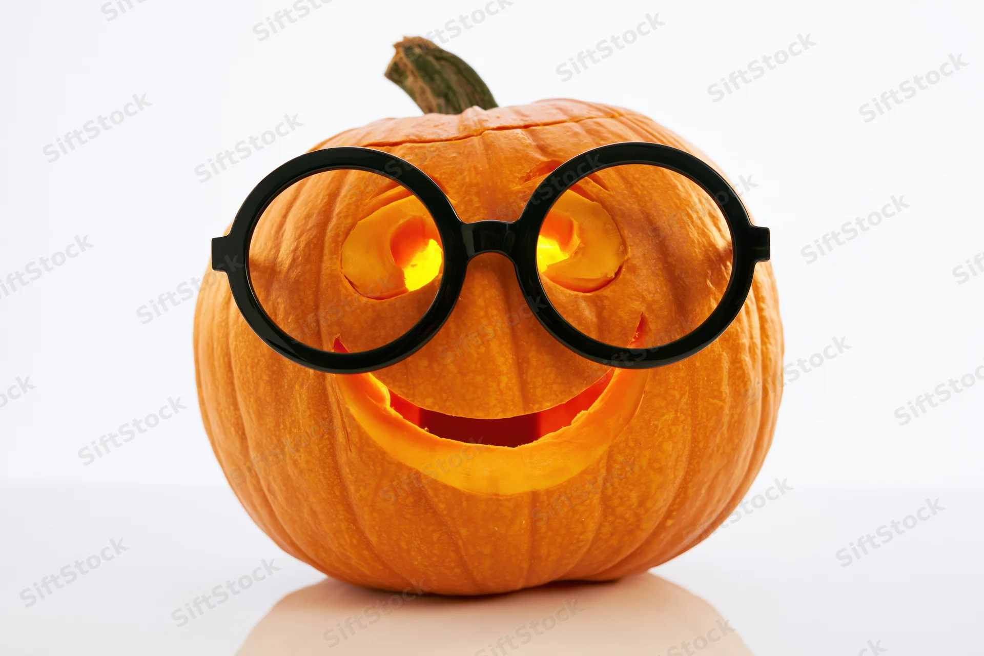 Carved pumpkin with smiling face and oversized glasses glowing from within on white background