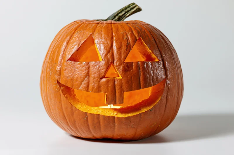 Carved pumpkin with triangular eyes and smiling mouth lit from within on white background