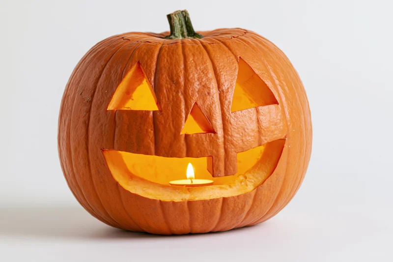 Carved pumpkin with triangular eyes and smiling mouth lit by candle on white background