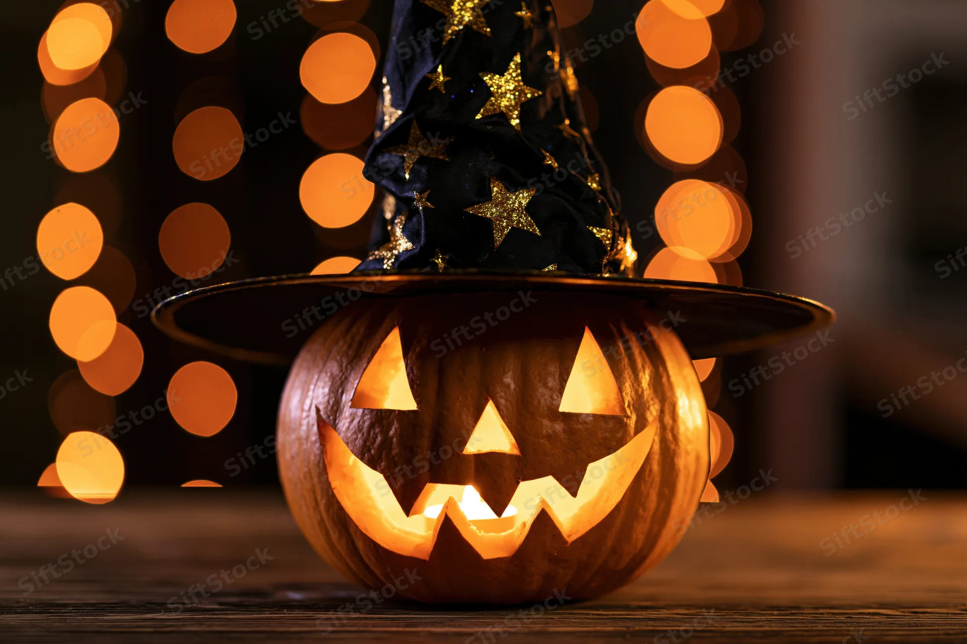 Carved pumpkin with witch hat glowing on wooden table at night