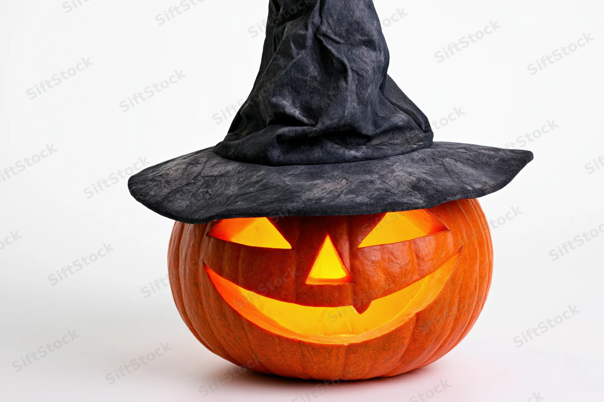 Carved jack-o-lantern with glowing face wearing a black witch hat on white background