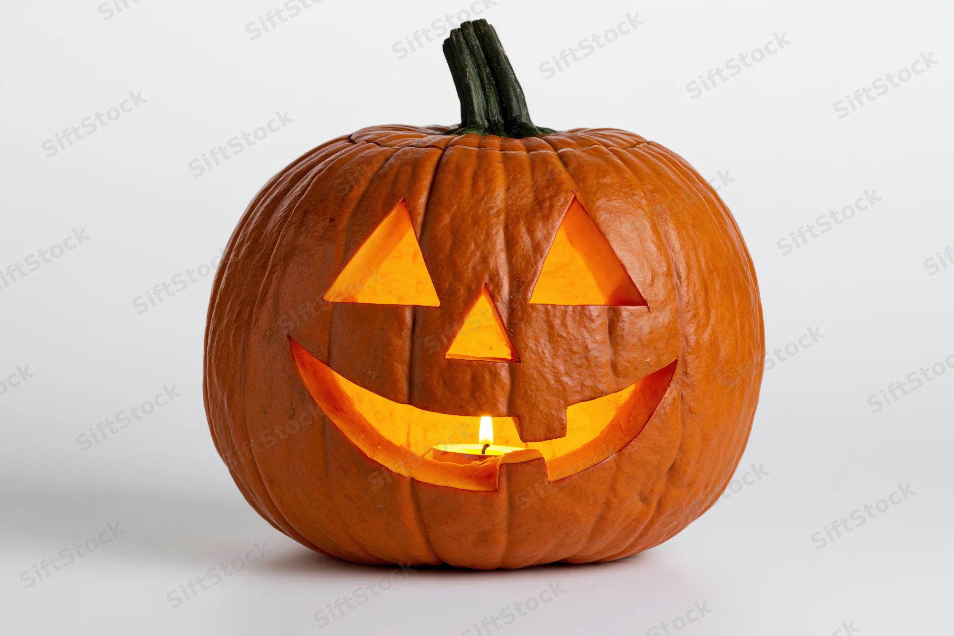 Carved pumpkin with triangular eyes and grin lit by candle on white background