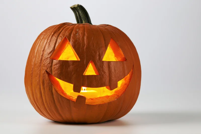 Carved pumpkin with triangular eyes and grin lit from within on white background
