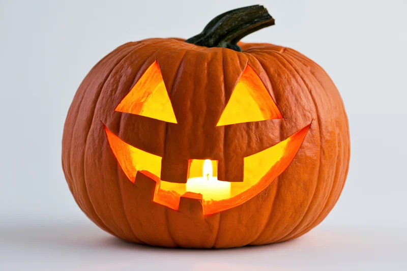 Carved pumpkin with triangular eyes and grinning mouth lit by candle on white background