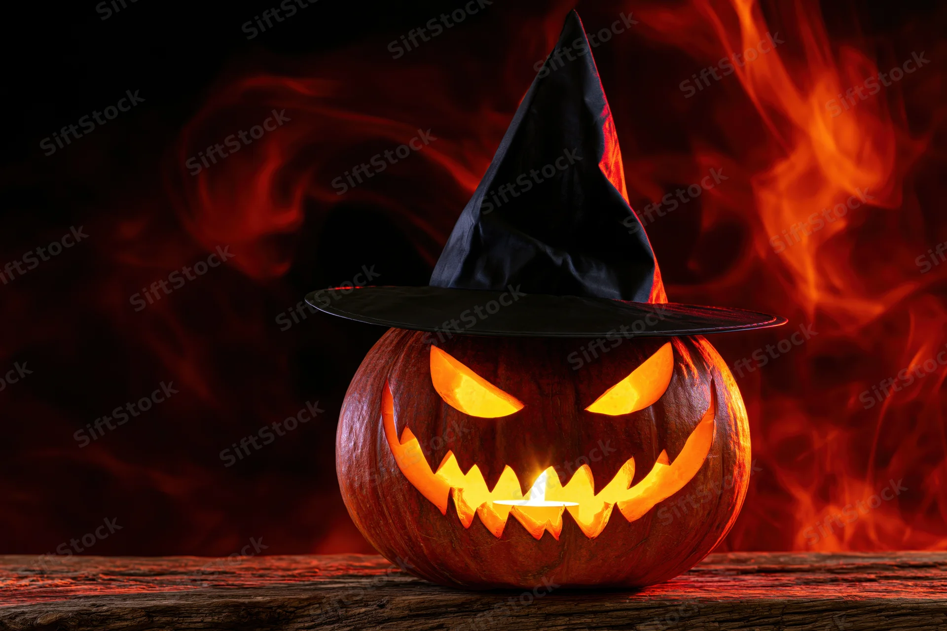 Carved jack-o-lantern with jagged grin and witch hat glowing on wooden table against fiery background