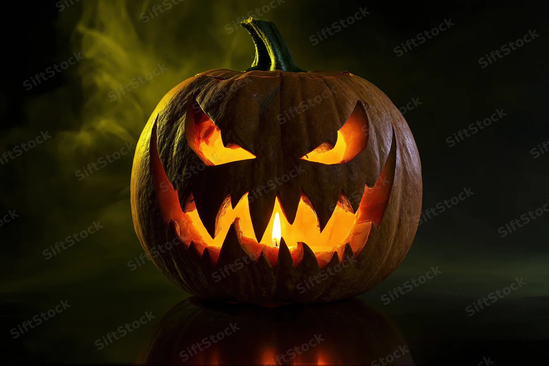Carved pumpkin with jagged grin lit by candle on dark reflective surface with smoke