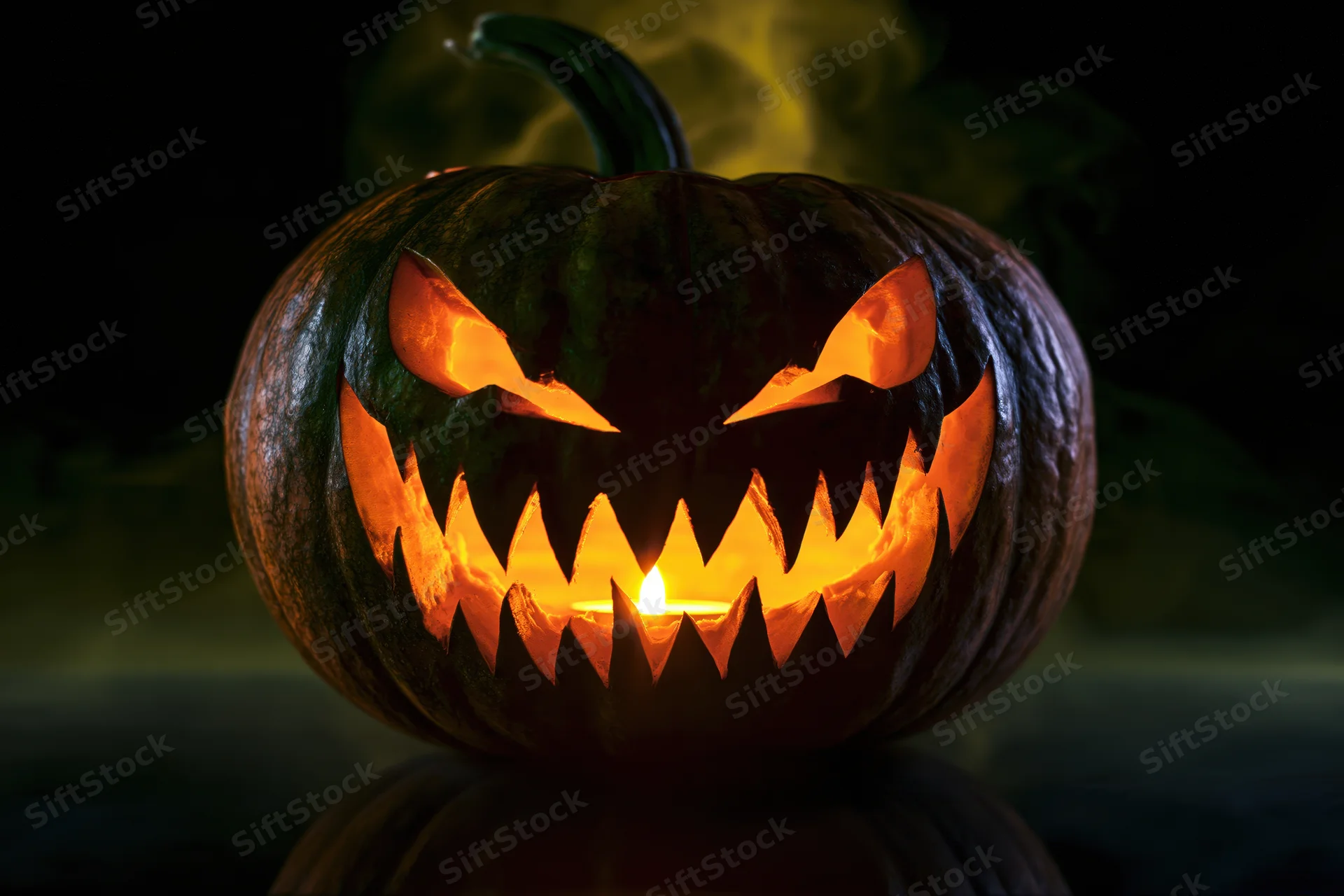 Carved pumpkin with jagged grin illuminated by candlelight in dark setting
