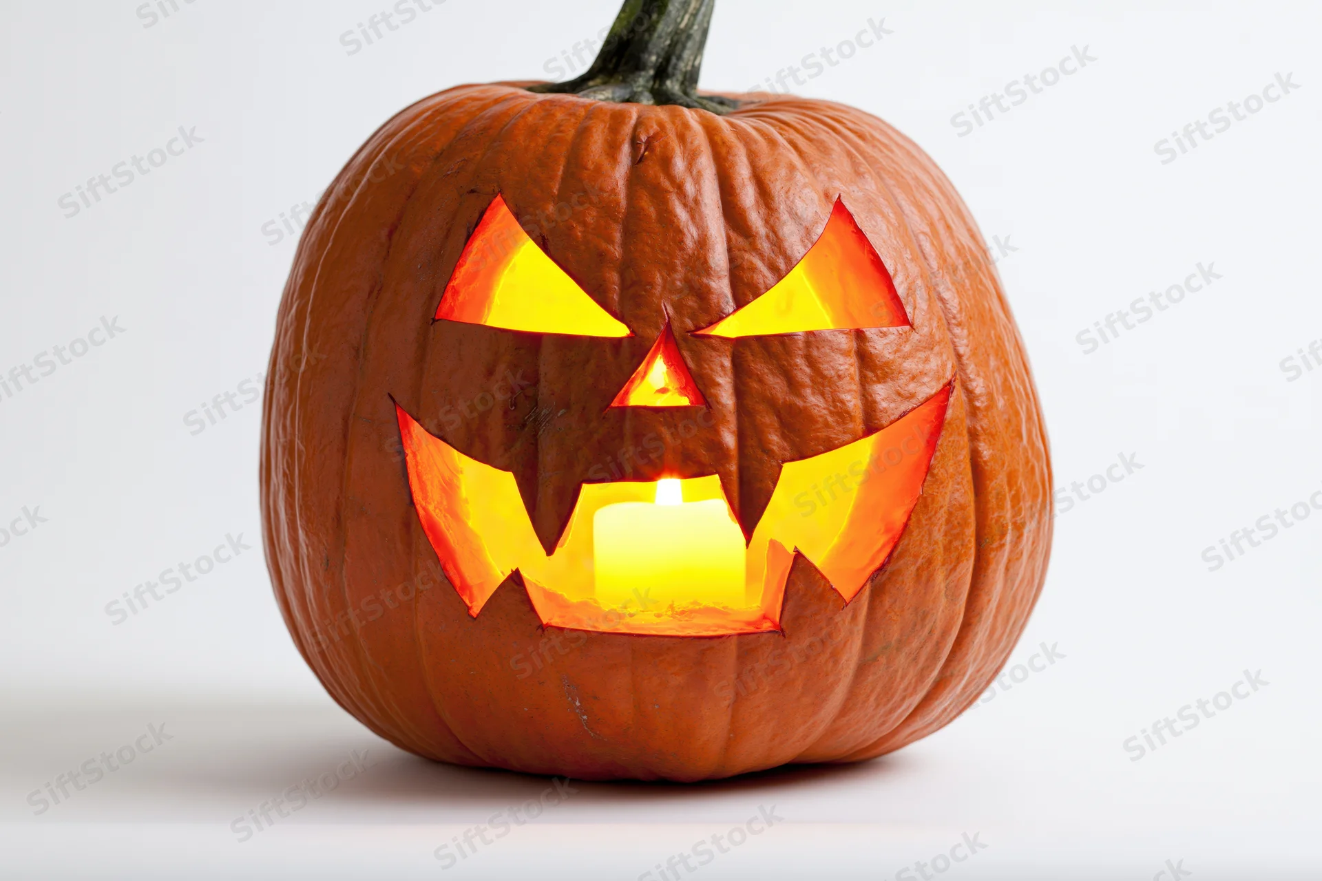 Carved pumpkin with glowing candle inside, set against white background