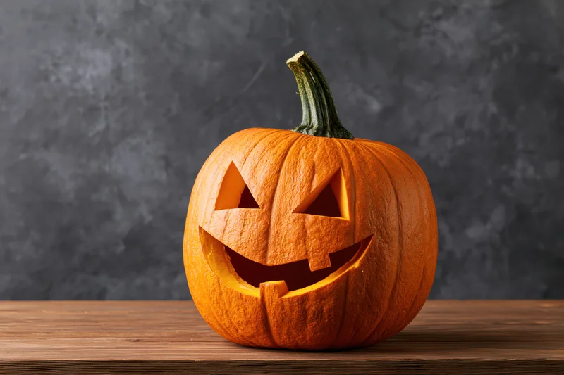 Carved pumpkin with smiling triangular eyes and mouth on wooden table against dark background