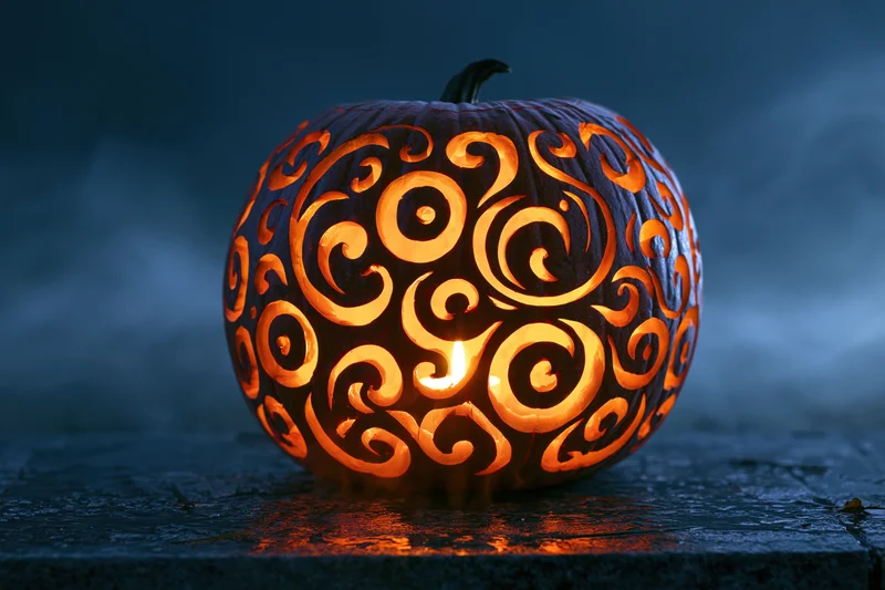 Carved pumpkin with swirling filigree pattern glowing in the dark on a stone surface